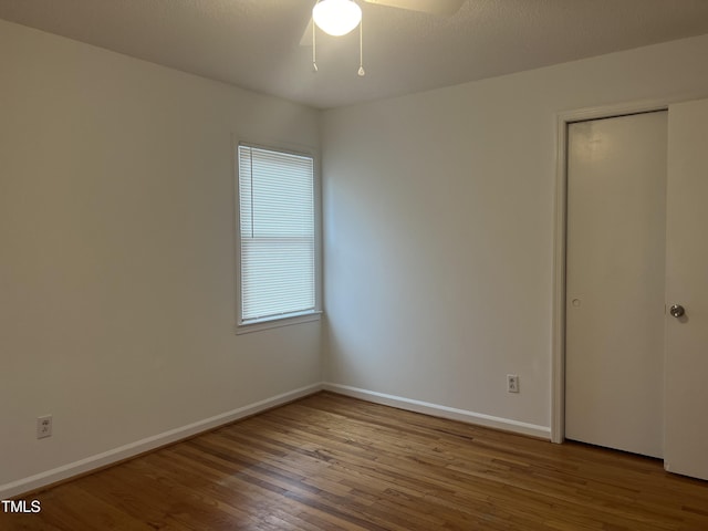 unfurnished bedroom with a closet, wood finished floors, a ceiling fan, and baseboards