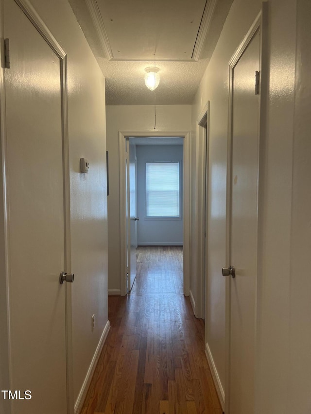 hall with a textured ceiling, wood finished floors, attic access, and baseboards