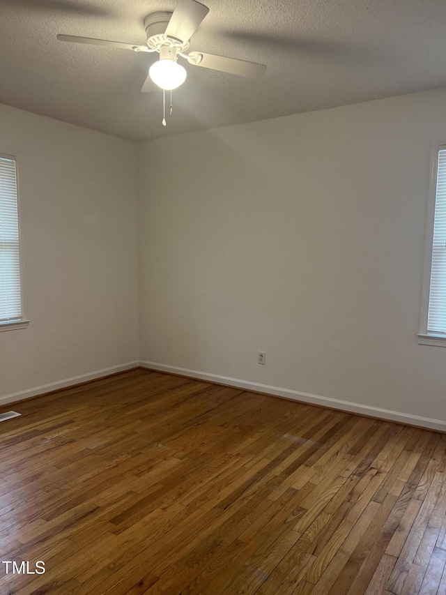 spare room with baseboards, visible vents, a ceiling fan, wood-type flooring, and a textured ceiling