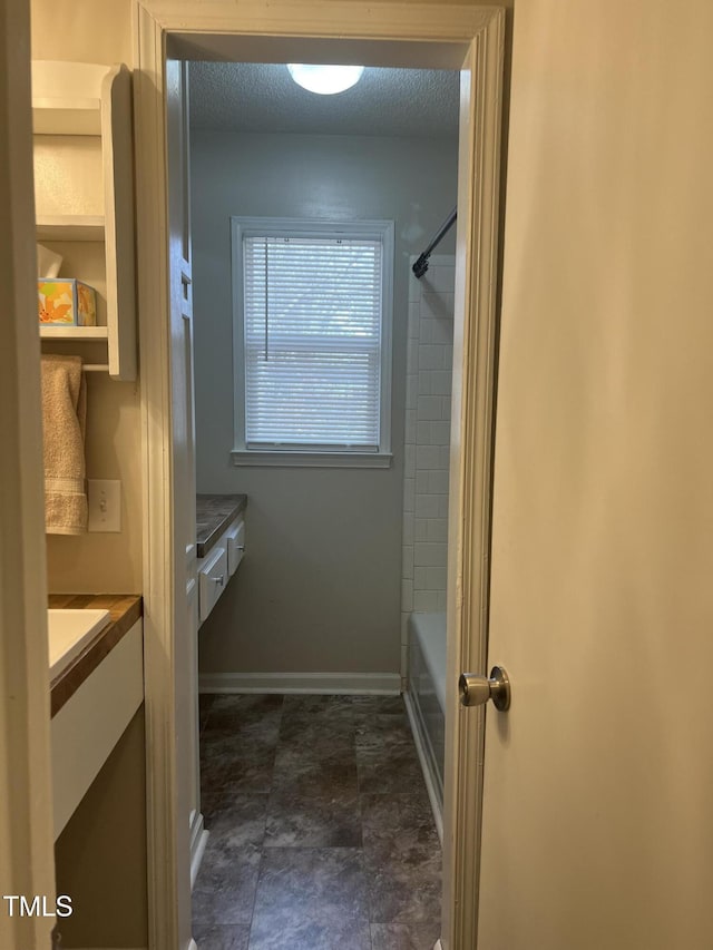 bathroom featuring bathing tub / shower combination, baseboards, a textured ceiling, and vanity