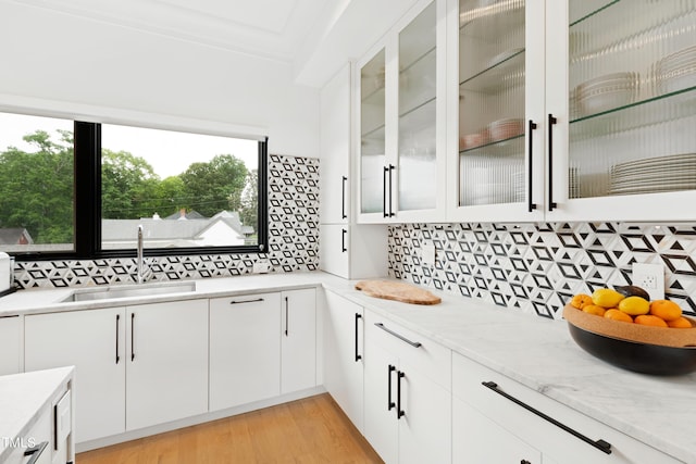 kitchen featuring sink, backsplash, ornamental molding, white cabinets, and light wood-type flooring