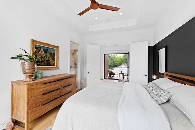 bedroom featuring hardwood / wood-style flooring, ceiling fan, access to exterior, connected bathroom, and a tray ceiling