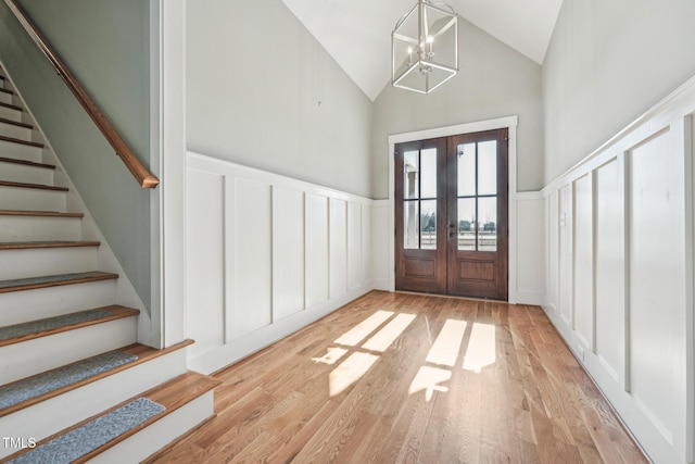 entrance foyer with high vaulted ceiling, a notable chandelier, light wood-type flooring, and french doors