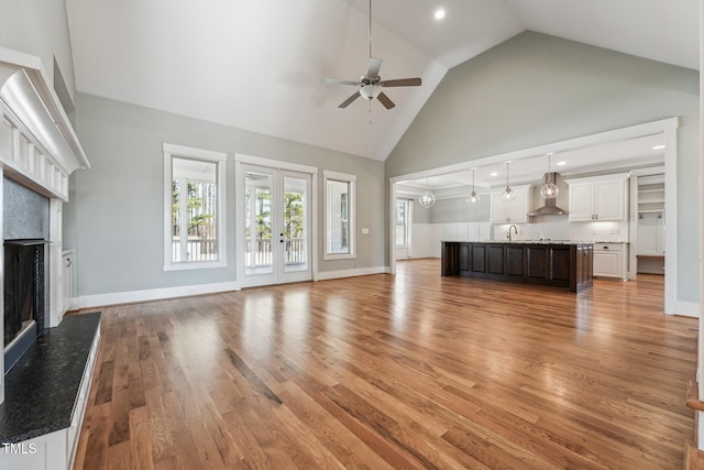 unfurnished living room featuring high vaulted ceiling, wood-type flooring, sink, ceiling fan, and a premium fireplace