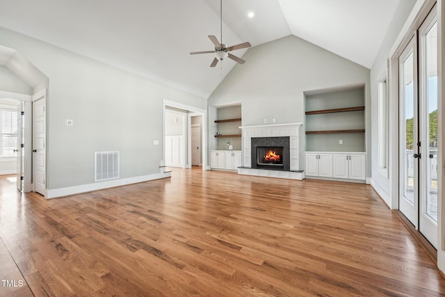 unfurnished living room featuring a tiled fireplace, wood-type flooring, plenty of natural light, and built in features