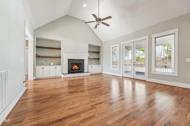 unfurnished living room with a fireplace, ceiling fan, light hardwood / wood-style floors, built in shelves, and french doors