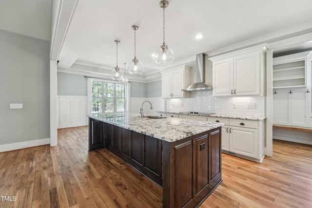 kitchen featuring pendant lighting, wall chimney range hood, light stone counters, and white cabinets