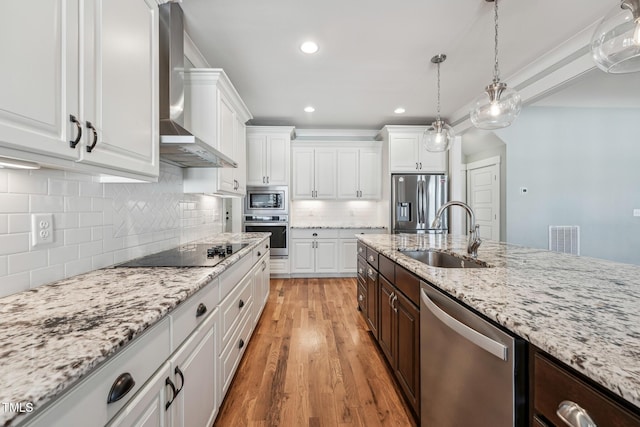 kitchen featuring sink, wall chimney range hood, white cabinetry, hanging light fixtures, and stainless steel appliances