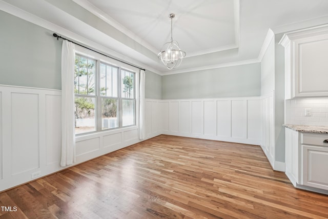 unfurnished dining area featuring a chandelier, ornamental molding, a raised ceiling, and light hardwood / wood-style flooring