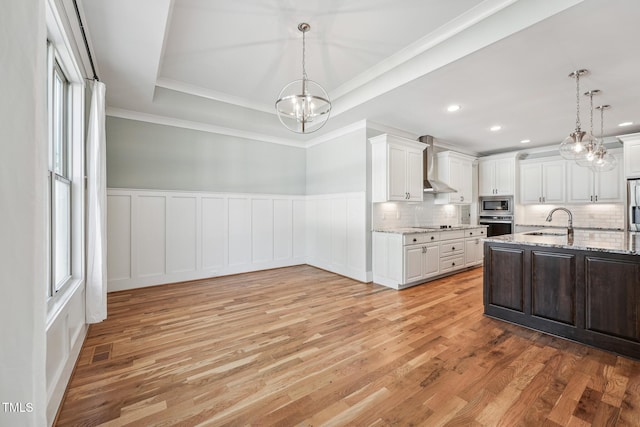 kitchen with decorative light fixtures, a raised ceiling, stainless steel appliances, light stone countertops, and white cabinets