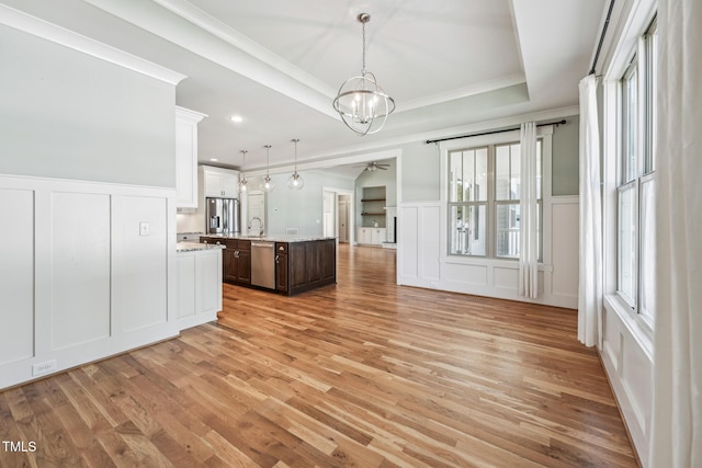 kitchen with sink, stainless steel appliances, dark brown cabinetry, a tray ceiling, and an island with sink