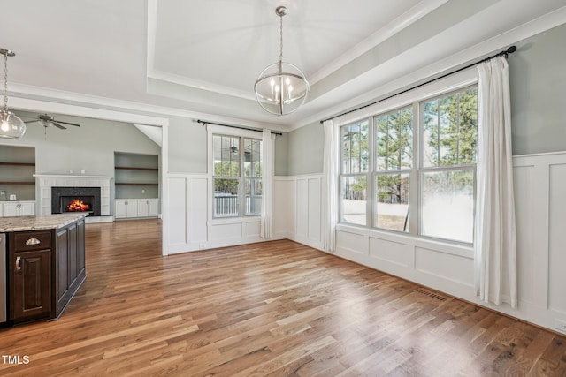 dining area featuring hardwood / wood-style flooring, ornamental molding, ceiling fan with notable chandelier, and a tray ceiling