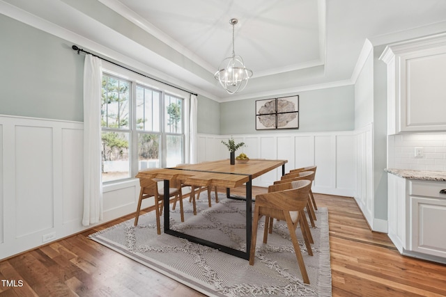 dining area featuring a chandelier, ornamental molding, a raised ceiling, and light hardwood / wood-style flooring