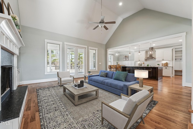 living room with french doors, high vaulted ceiling, ceiling fan, a high end fireplace, and light hardwood / wood-style floors