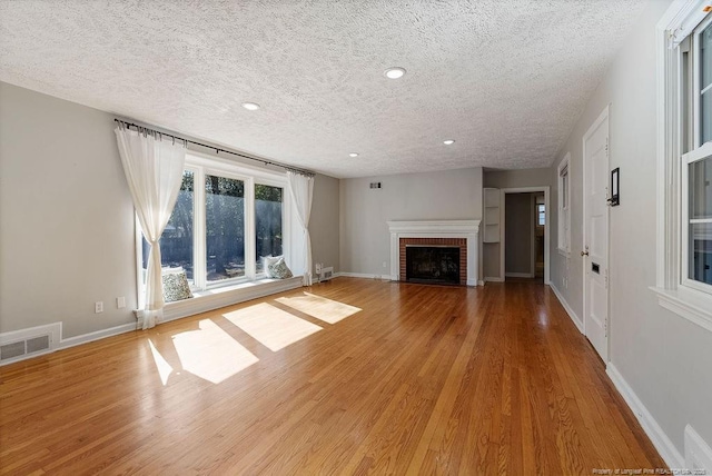 unfurnished living room featuring a brick fireplace, a textured ceiling, and light wood-type flooring