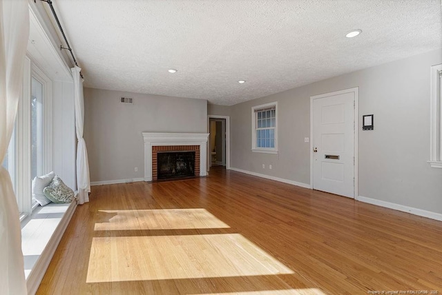 unfurnished living room featuring a fireplace, a textured ceiling, and light wood-type flooring