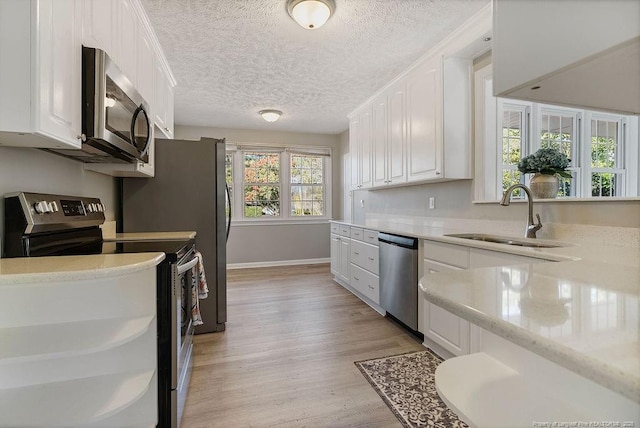 kitchen featuring white cabinetry, sink, light stone counters, stainless steel appliances, and light hardwood / wood-style flooring