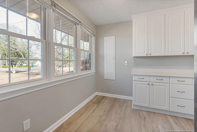 interior space with a textured ceiling, light hardwood / wood-style flooring, and white cabinets