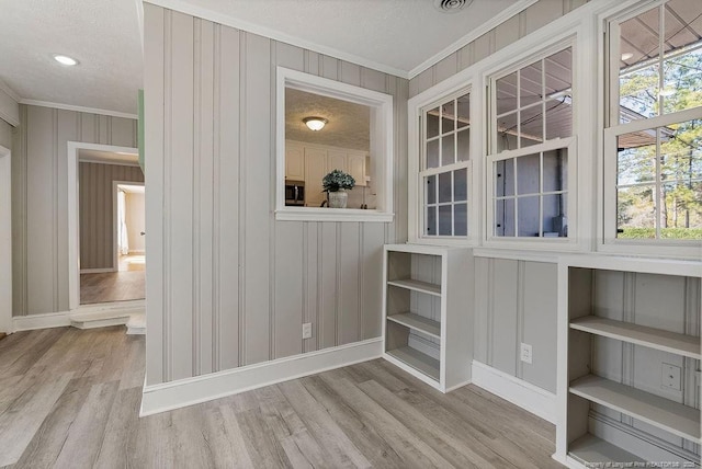 interior space with ornamental molding, a textured ceiling, and light wood-type flooring