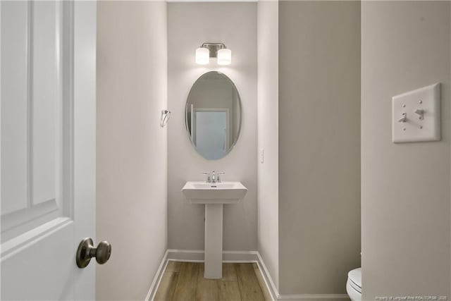 half bath with toilet, baseboards, and wood finished floors