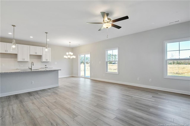 unfurnished living room featuring light wood-style flooring, visible vents, baseboards, and ceiling fan with notable chandelier