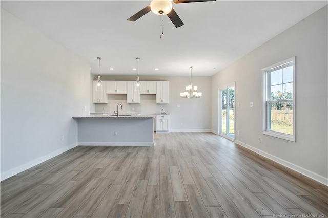 unfurnished living room with recessed lighting, a sink, wood finished floors, baseboards, and ceiling fan with notable chandelier