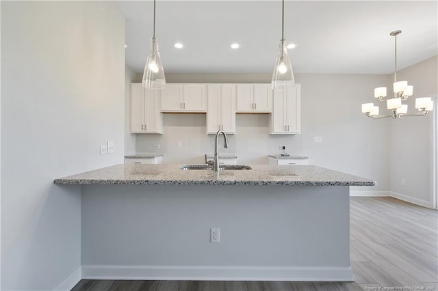 kitchen featuring a peninsula, light stone countertops, white cabinets, and a sink