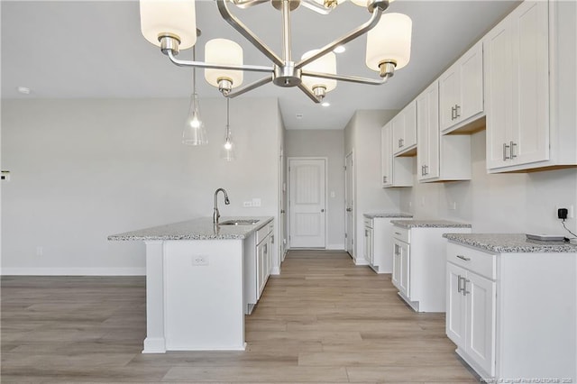 kitchen with a chandelier, light stone countertops, light wood-style floors, white cabinetry, and a sink