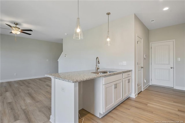 kitchen featuring white cabinets, open floor plan, light stone countertops, light wood-type flooring, and a sink