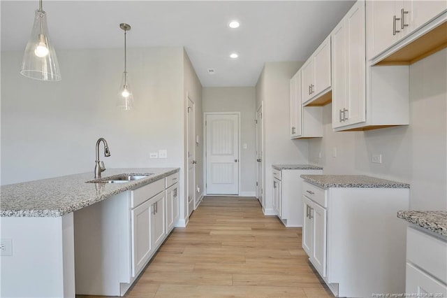 kitchen featuring light stone counters, a sink, light wood-style flooring, and white cabinets