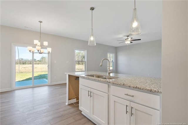 kitchen with white cabinets, light wood-style flooring, light stone counters, a sink, and ceiling fan with notable chandelier