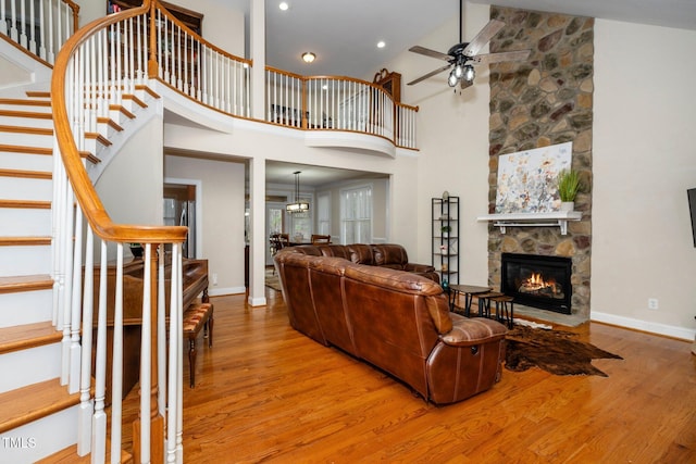 living room featuring a stone fireplace, light hardwood / wood-style flooring, ceiling fan, and a high ceiling