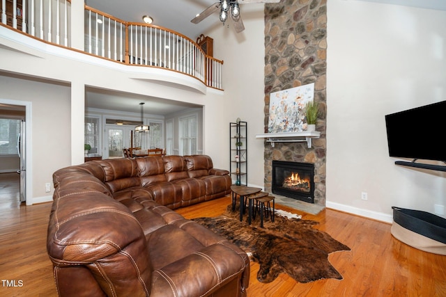 living room with ceiling fan, wood-type flooring, a fireplace, and a high ceiling