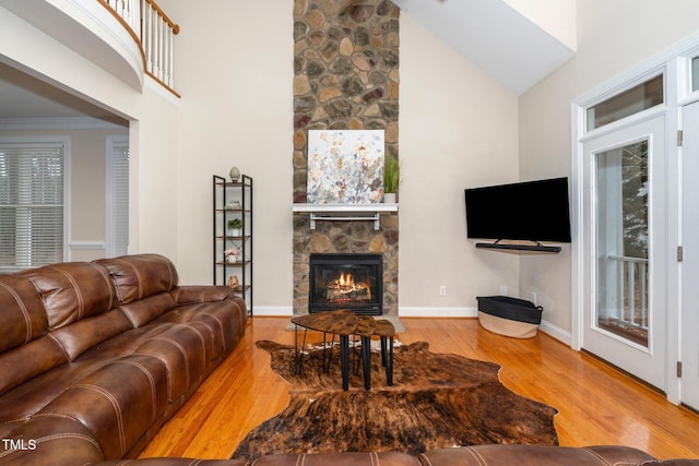 living room with crown molding, high vaulted ceiling, a fireplace, and light hardwood / wood-style flooring