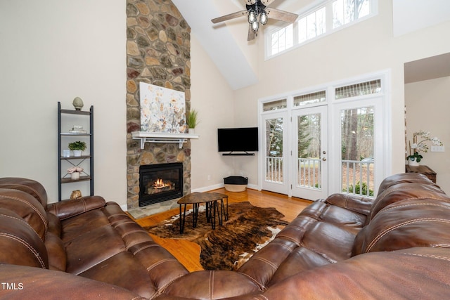 living room featuring ceiling fan, a towering ceiling, a stone fireplace, and light hardwood / wood-style floors