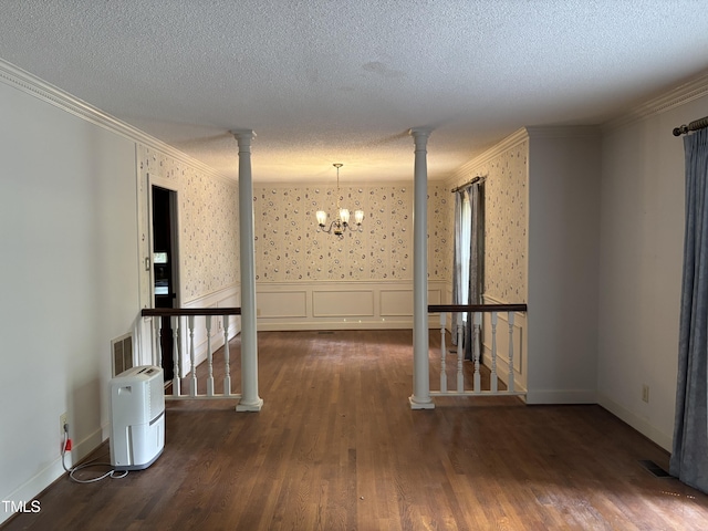 spare room featuring ornamental molding, a chandelier, wood finished floors, a textured ceiling, and ornate columns