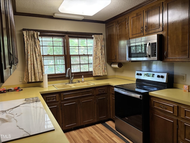 kitchen featuring appliances with stainless steel finishes, a sink, a textured ceiling, light countertops, and ornamental molding
