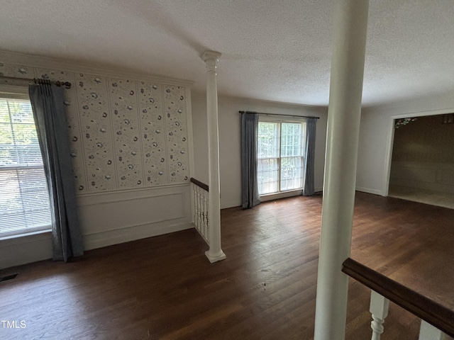 empty room featuring dark wood-type flooring, decorative columns, and a textured ceiling