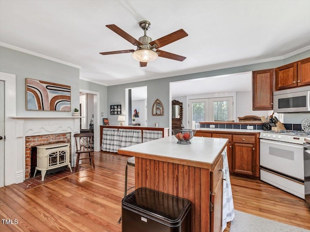 967 Bynum Rd, Pittsboro, NC 27312 - kitchen featuring white range with gas stovetop, a wood stove, light wood-style flooring, a ceiling fan, and ornamental molding
