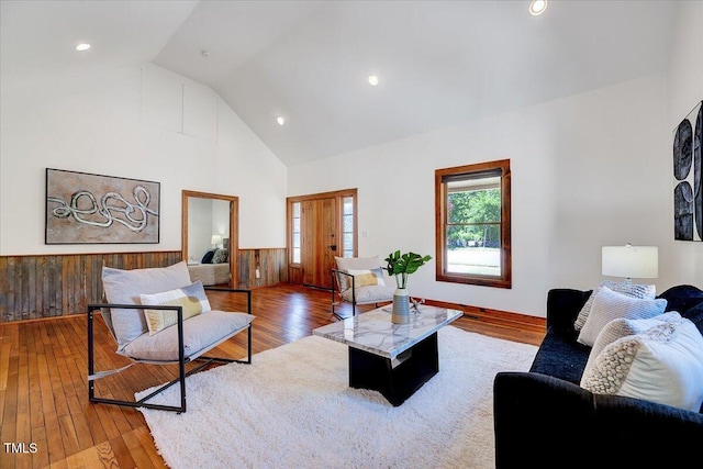 living room with high vaulted ceiling, hardwood / wood-style floors, and wooden walls