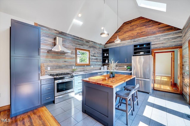 kitchen featuring a kitchen island, appliances with stainless steel finishes, wood counters, a kitchen breakfast bar, and wall chimney exhaust hood