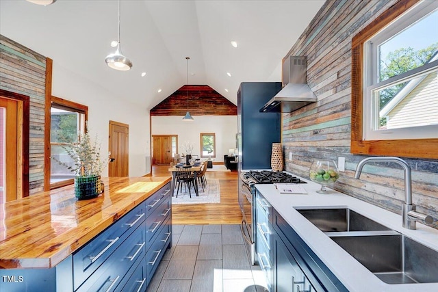 kitchen with wood counters, sink, gas stove, decorative light fixtures, and exhaust hood