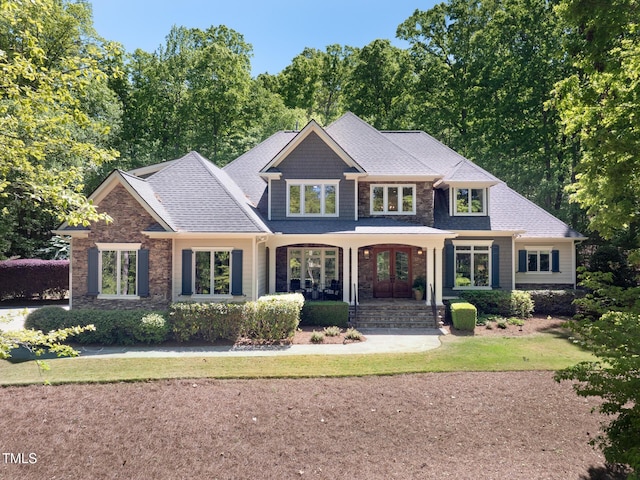 craftsman inspired home featuring a porch, a shingled roof, and stone siding