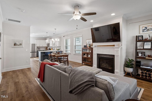 living room with hardwood / wood-style flooring, crown molding, and ceiling fan with notable chandelier