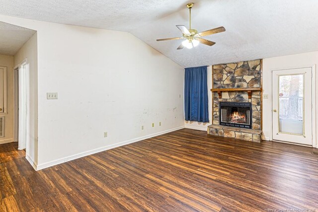 unfurnished living room featuring a stone fireplace, lofted ceiling, ceiling fan, dark wood-type flooring, and a textured ceiling