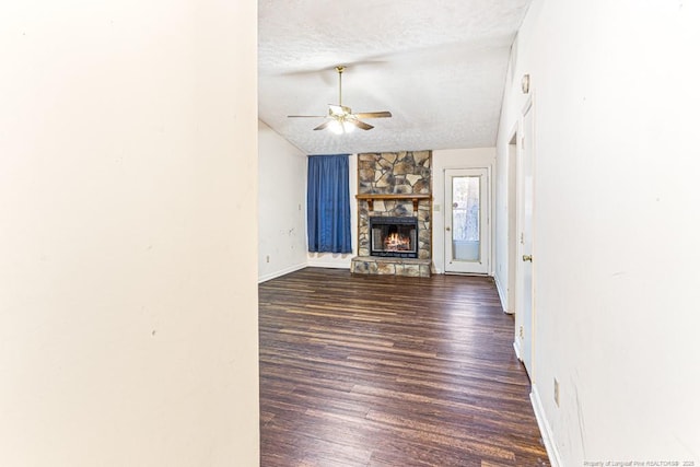 unfurnished living room with ceiling fan, lofted ceiling, a stone fireplace, wood finished floors, and a textured ceiling