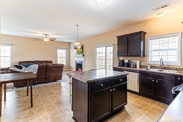 kitchen featuring sink, dishwasher, decorative backsplash, a kitchen island, and decorative light fixtures