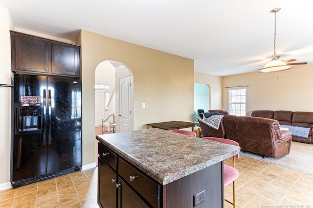 kitchen with ceiling fan, dark brown cabinets, a center island, a kitchen bar, and black fridge with ice dispenser