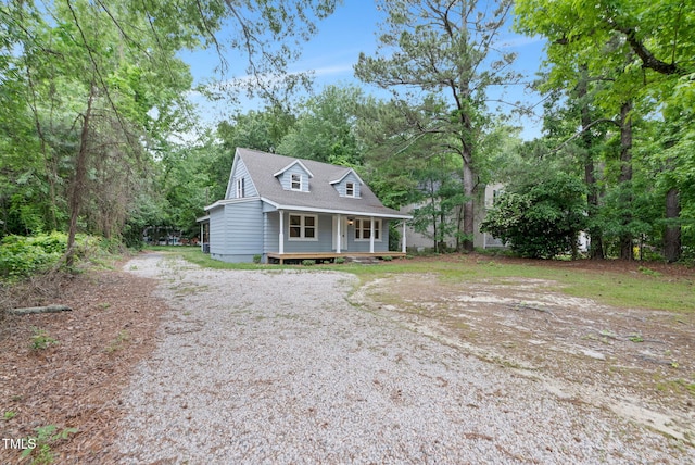 view of front of property with gravel driveway, a porch, and view of wooded area
