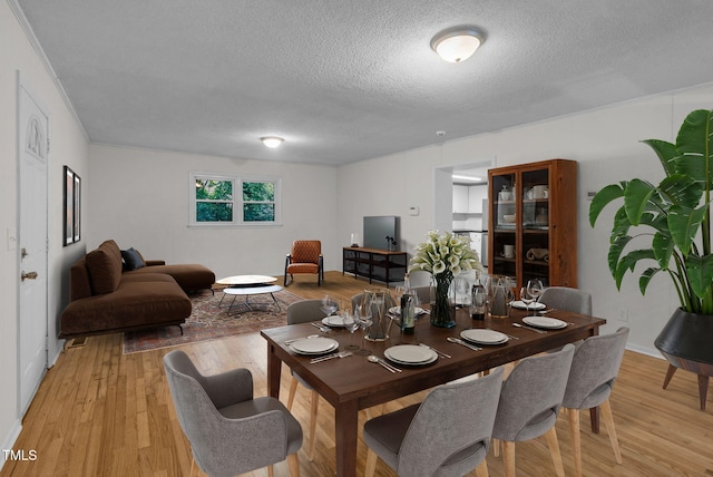dining space featuring a textured ceiling, light wood finished floors, and baseboards